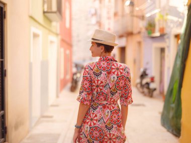 İspanyol kıyı kasabası La Vila Joiosa 'nın renkli sokaklarında gezen kadın. Güneşli kış atmosferi Akdeniz mimarisinin cazibesini ve sakin sahil yaşamını ön plana çıkarıyor.