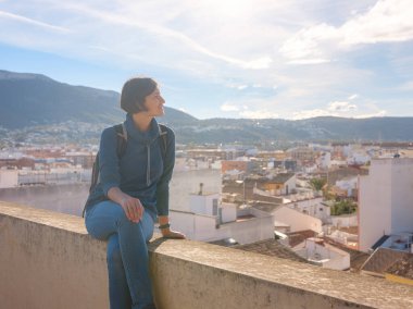 Denia, Alicante, İspanya 'da tarihi şatoyu keşfeden genç bir kadın, aşağıdaki kasabanın manzarası, daha serin mevsim arkaplanlarına karşı. Tarihin ve sükunetin zamansız ortamında harmanlanması.