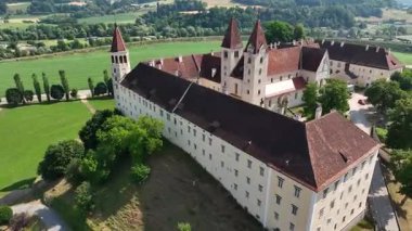 Sankt Paul im Lavanttal 'ın yaz havası manastır kompleksi, çatılar, vadi manzarası, yeşil tepeler, sakin sinema insansız hava aracı hareketi, sıcak atmosfer tonları.