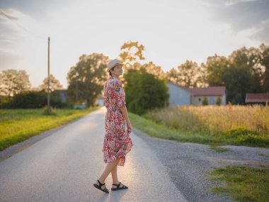 Yaz sonlarında Avrupa 'nın pitoresk alanlarında yürüyen genç bir kadın. Altın güneş ışığı, yemyeşil yemyeşil ve sakin kırsal atmosfer huzurlu bir kırsal alan yaratır..
