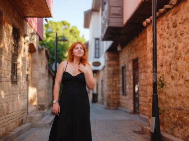 Zarif siyah elbiseli genç bir kadın yaz günü Türkiye 'nin Keleci, Antalya kentinde yürüyor. Kadın gezgin ilginç yerler ve popüler yerler keşfediyor.