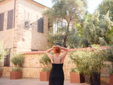 Zarif siyah elbiseli genç bir kadın yaz günü Türkiye 'nin Keleci, Antalya kentinde yürüyor. Kadın gezgin ilginç yerler ve popüler yerler keşfediyor.