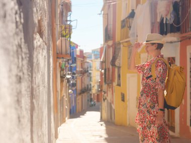İspanyol kıyı kasabası La Vila Joiosa ya da Villajoyosa 'nın renkli caddelerinde gezen kadın. Güneşli kış atmosferi Akdeniz mimarisinin ve sakin deniz yaşamının cazibesini vurguluyor