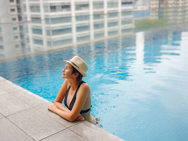 Kuala Lumpur Oteli 'nde havuz başında dinlenen Asyalı genç bir kadın. Etrafı gökdelenlerle çevrili, hareketli şehir ortamında boş vakitlerin tadını çıkarıyor..