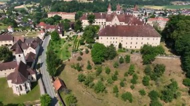 Sankt Paul im Lavanttal 'ın yaz havası manastır kompleksi, çatılar, vadi manzarası, yeşil tepeler, sakin sinema insansız hava aracı hareketi, sıcak atmosfer tonları.