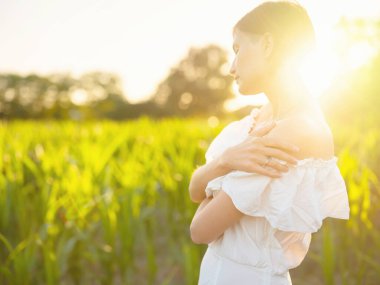 Hırvatistan 'da yaz günbatımında beyaz elbiseli güzel bir kadın, sıcak güneş ışığı, romantik akşam havası, doğal kırsal atmosfer, yumuşak rüzgar ve huzurlu manzara.