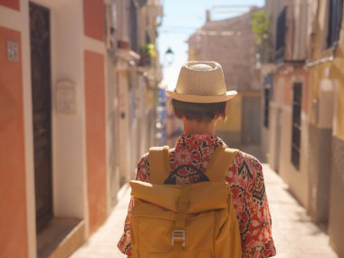 İspanyol kıyı kasabası La Vila Joiosa 'nın renkli sokaklarında gezen kadın. Güneşli kış atmosferi Akdeniz mimarisinin cazibesini ve sakin sahil yaşamını ön plana çıkarıyor.