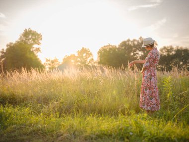 Yaz sonlarında Avrupa 'nın pitoresk alanlarında yürüyen genç bir kadın. Altın güneş ışığı, yemyeşil yemyeşil ve sakin kırsal atmosfer huzurlu bir kırsal alan yaratır..