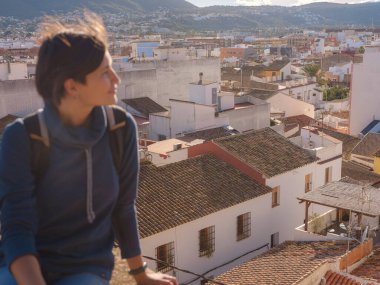 Denia, Alicante, İspanya 'da tarihi şatoyu keşfeden genç bir kadın, aşağıdaki kasabanın manzarası, daha serin mevsim arkaplanlarına karşı. Tarihin ve sükunetin zamansız ortamında harmanlanması.