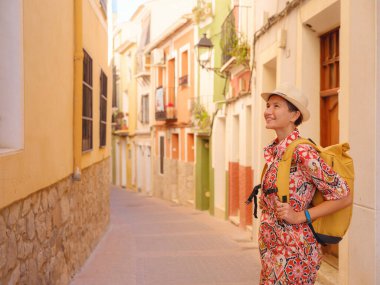 İspanyol kıyı kasabası La Vila Joiosa ya da Villajoyosa 'nın renkli caddelerinde gezen kadın. Güneşli kış atmosferi Akdeniz mimarisinin ve sakin deniz yaşamının cazibesini vurguluyor