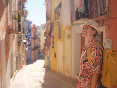 İspanyol kıyı kasabası La Vila Joiosa ya da Villajoyosa 'nın renkli caddelerinde gezen kadın. Güneşli kış atmosferi Akdeniz mimarisinin ve sakin deniz yaşamının cazibesini vurguluyor