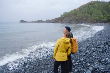 Çiftler Türk kıyı şeridini seviyor. Taşlarda oturmak, deniz dalgalarını izlemek, birlikte dinlenmek, sakin mavi suyun yanında, yumuşak kış ışığı altında romantik bir an..