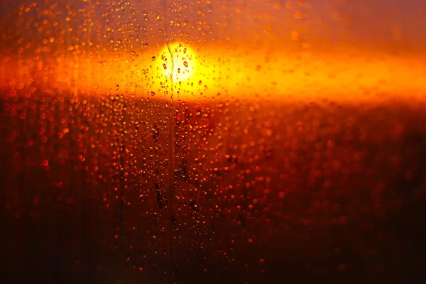 Gotas de agua en un vaso de ventana después de la lluvia. El cielo con nubes y el sol en el fondo . — Foto de Stock
