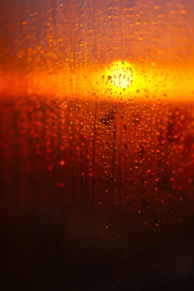 Gotas de agua en un vaso de ventana después de la lluvia. El cielo con nubes y el sol en el fondo . — Foto de Stock