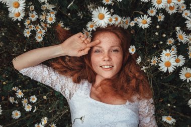 Papatya alanındaki kıvırcık kırmızı saçlı güzel genç kız