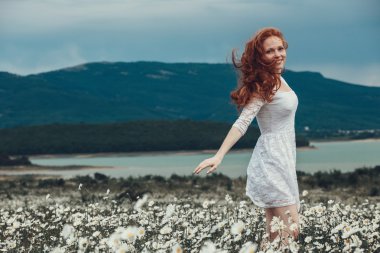 Papatya alanındaki kıvırcık kırmızı saçlı güzel genç kız