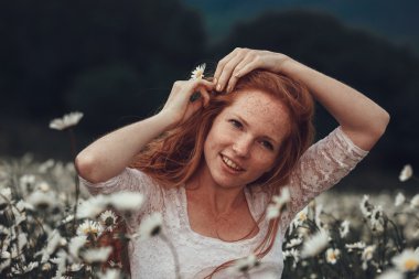 Papatya alanındaki kıvırcık kırmızı saçlı güzel genç kız