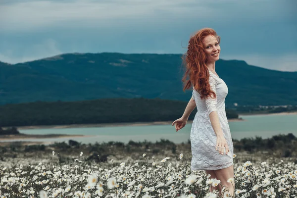 Beautiful young girl with curly red hair in chamomile field — Stock Photo, Image