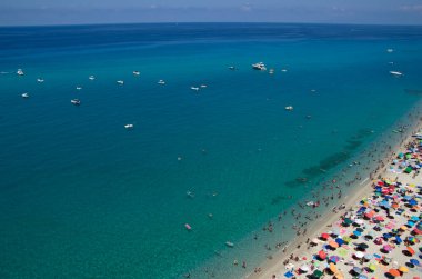 Turkuvaz suyu ve kumu olan deniz plajı insanların dinlendiği, yüzdüğü ve şemsiyelerle güneşlendiği yer.