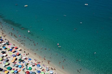 Yazın şeffaf mavi suyla yüzen insanların olduğu kumlu sahil manzarası. Üst Manzara. Peyzaj