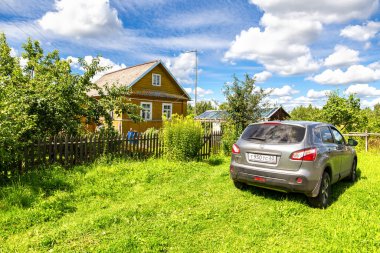 Borovichi, Rusya - 6 Ağustos 2020: Nissan Kashqai arabasının yaz günü park edildiği Rus köyünde küçük bir kırsal ahşap ev