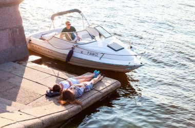 Saint Petersburg, Rusya - 27 Ağustos 2016: İki genç kız, demirli bir motorlu teknenin yanındaki granit barajda dinleniyor