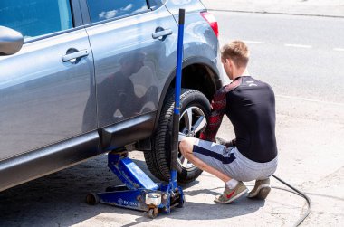 Samara, Rusya - 4 Temmuz 2021: Tamirci aracı tamir ediyor. Tamirci, tekerleği ingiliz anahtarıyla, lastik montaj ekipmanlarıyla kaldırıyor. Adam arabayı tamir ediyor. Lastik uydurma kavramı