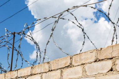 Çitin üzerindeki dikenli teller mavi gökyüzü arka planına karşı. Hapishane duvarı