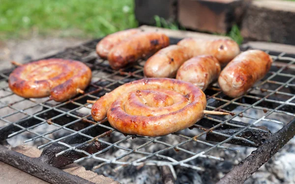 Salsichas saborosas cozinhando sobre as brasas em um fogo de churrasco — Fotografia de Stock