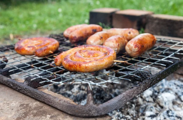 Saucisses savoureuses cuisson sur les charbons chauds sur un feu de barbecue — Photo