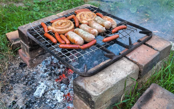 Deliciosas salsichas em uma grade de metal grelhando sobre carvão quente para um — Fotografia de Stock