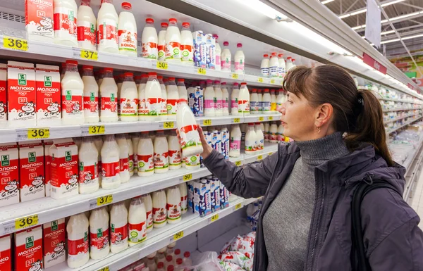 Young woman choosing fresh milk produces at shopping in dairy su — Stock Photo, Image