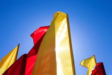 Rüzgara karşı mavi gökyüzü içinde çırpınan kırmızı ve sarı bayrak