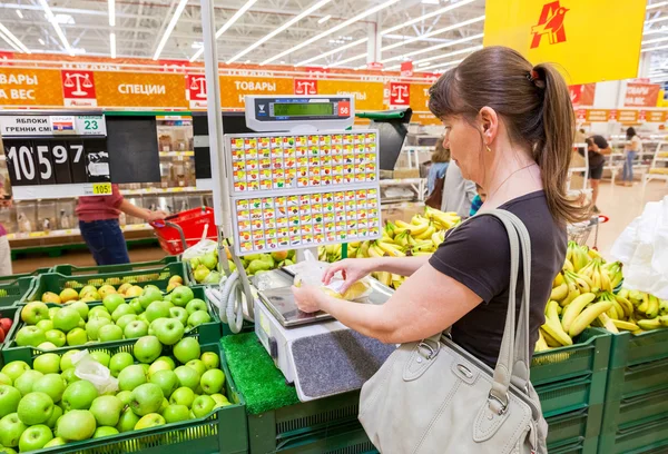 Young woman weighing bananas on electronic scales in produce dep — Stock Photo, Image