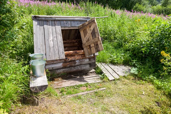 Pozo de agua de madera del pueblo con la puerta abierta y un cubo de wa — Foto de Stock