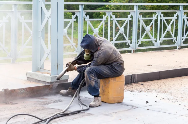 Lucrătorul în haine de protecție curăță structurile metalice sandbla — Fotografie, imagine de stoc