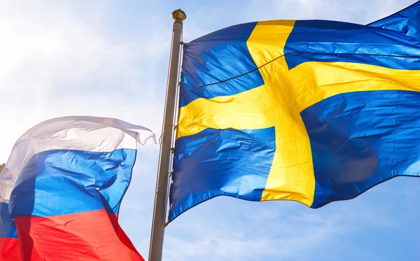 Flags of Sweden and Russia waving against blue sky — Stock Photo, Image