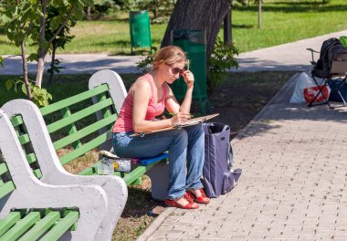 Bir şehir parkta bir bankta oturan kız çizer