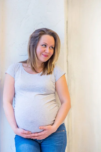 Vacker gravid kvinna står nära fönstret hemma i ljus interiör — Stockfoto