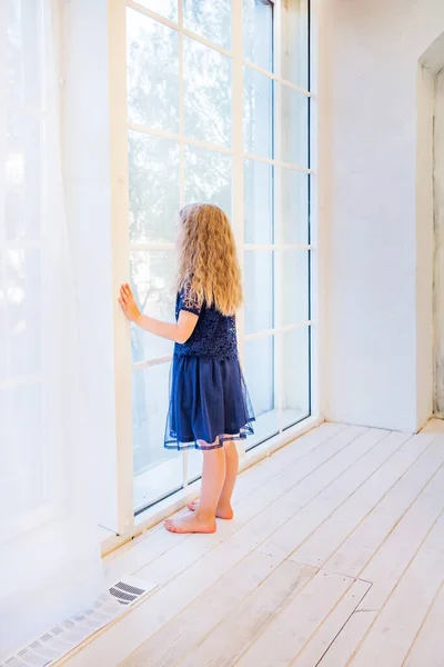 Menina bonito em roupas casuais de pé perto da janela e olhando para fora — Fotografia de Stock