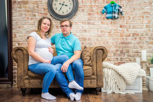 Beautiful pregnant woman and man sitting near wall — Stock Photo, Image