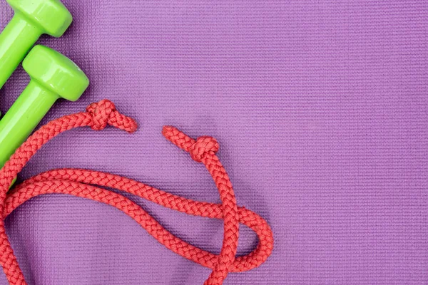 Ladies dumbbles and skipping rope over purple fitness mat, top view. — Stock Photo, Image