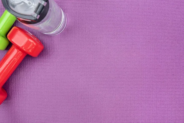 Manivelas de las señoras y botella de agua sobre la estera de fitness púrpura, vista superior. — Foto de Stock