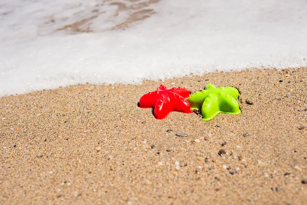 Red and green starfish-shaped molds on the sand — Stock Photo, Image