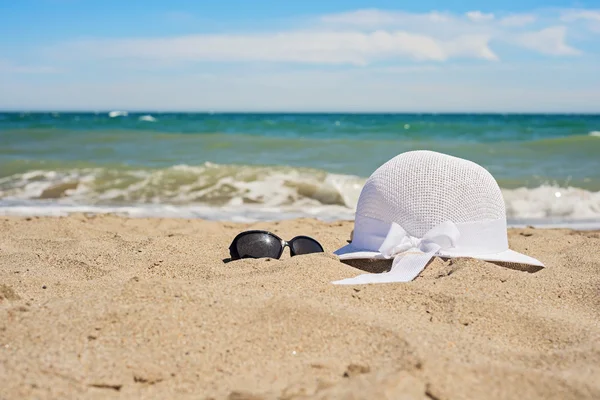 Gorro blanco de mimbre y gafas de sol en la playa — Foto de Stock