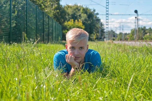 Jonge man in blauw t-shirt liggend op het groene gras — Stockfoto