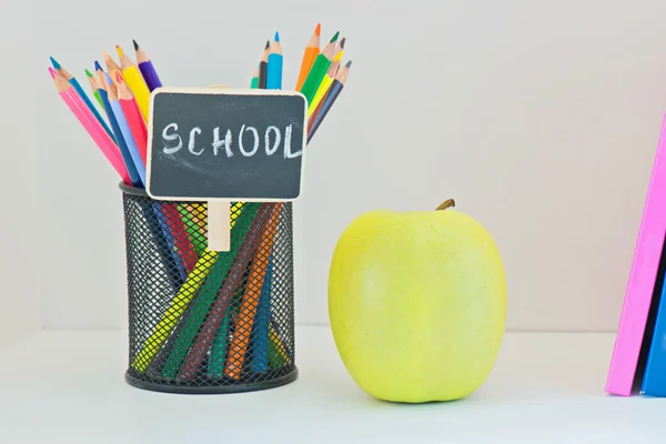 Yellow apple, pencils in case and multi colored books — Stock Photo, Image