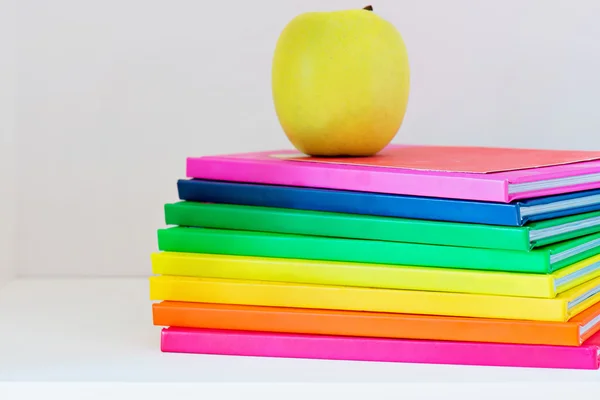 Una manzana amarilla sentada encima de una pila de libros escolares — Foto de Stock