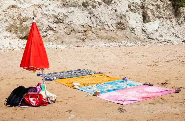 Strandtörölközők és piros esernyő, a homok, a tenger közelében — Stock Fotó
