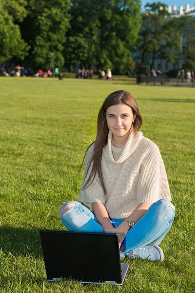 Mujer joven en una hierba en el parque o jardín utilizando el ordenador portátil —  Fotos de Stock